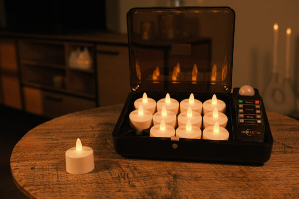 12 vandtætte genopladelige LED-fyrfadslys i sort opladningskuffert på træbord – ét lys udenfor, med stemningsfuldt rum i baggrunden