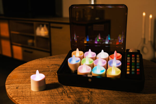 12 RGB LED-fyrfadslys fra DORSETTO i åben sort opladningsboks på rundt træbord med moderne stue i baggrunden