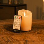 Genopladeligt LED-vokslys med bevægelig flamme Ø 7,5 x 10 cm i varm hvid på træbord med fjernbetjening og hyggelig baggrund