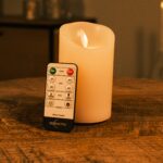 Genopladeligt LED-vokslys med bevægelig flamme Ø 7,5 x 12,5 cm i varm hvid på træoverflade med fjernbetjening