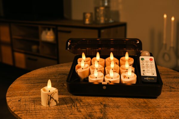 Et sæt med ni flammeløse LED-lys er anbragt i et sort opladningsetui på et træbord med en fjernbetjening ved siden af. Et ekstra lys sidder uden for kassen og lyser svagt.