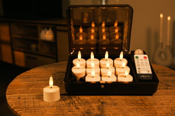 På et rundt træbord står et sæt flammeløse LED fyrfadslys og en fjernbetjening. Elleve lys er i et sort etui, og et lys står på bordet foran etuiet.