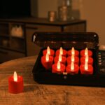 Tolv genopladelige røde LED-fyrfadslys står til opladning i en sort opladecase på et træbord; ét rødt lys ligger adskilt. Den hyggelige stue i baggrunden er dæmpet oplyst.