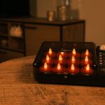 En sort ladestation med flere små, tændte LED-twistlys står på et træbord i et hyggeligt, svagt oplyst rum med dæmpet belysning og et træskab i baggrunden.