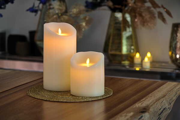 LED-vokslys i varm hvid fra DORSETTO med buede toppe på gylden flettet dækkeserviet omgivet af dekorationer for en varm stemning