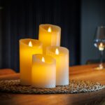 Fire genopladelige LED-vokslys fra DORSETTO i forskellige højder på en flettet måtte på et træbord med vin og varm baggrundsbelysning