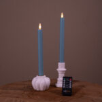 To stone blue LED-dinerlys (sæt med 2, op til 400 timers brændetid) i hvide holdere på en træoverflade med sort fjernbetjening foran, mod ensfarvet brun baggrund