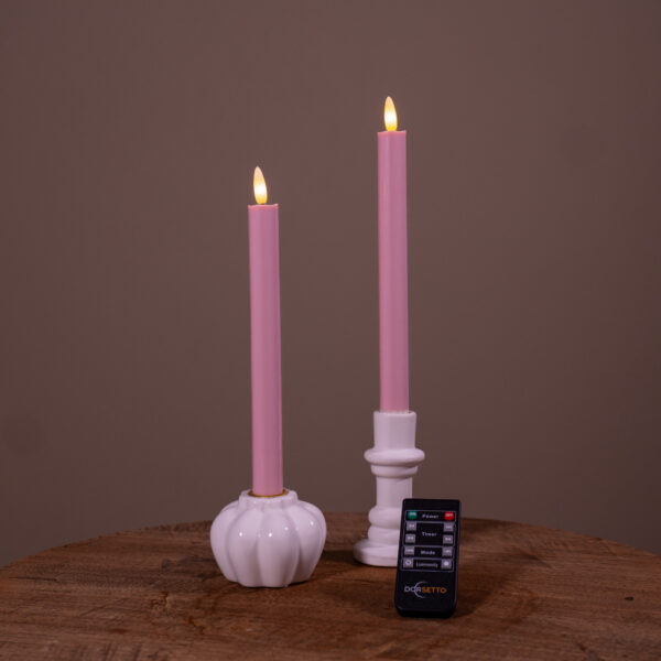 To lyserøde genopladelige LED middagslys (sæt med 2, 400 timers brændetid) i hvide holdere på en træoverflade, med en lille fjernbetjening foran og ensfarvet brun baggrund.