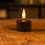 Lille batteridrevet LED-lys med varmt, flakkende skær placeret på en træoverflade og skaber en hyggelig stemning