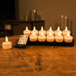 Tolv genopladelige fyrfadslys med realistiske 3D-flammer, 140 timers brændetid og fjernbetjening står på et træbord og giver et blødt, hyggeligt skær i baggrunden.