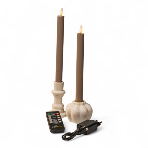 To beige, flammeløse LED-dinerlys i hvide lysestager, vist sammen med en sort fjernbetjening og en sort strømadapter, placeret mod en ensfarvet hvid baggrund.