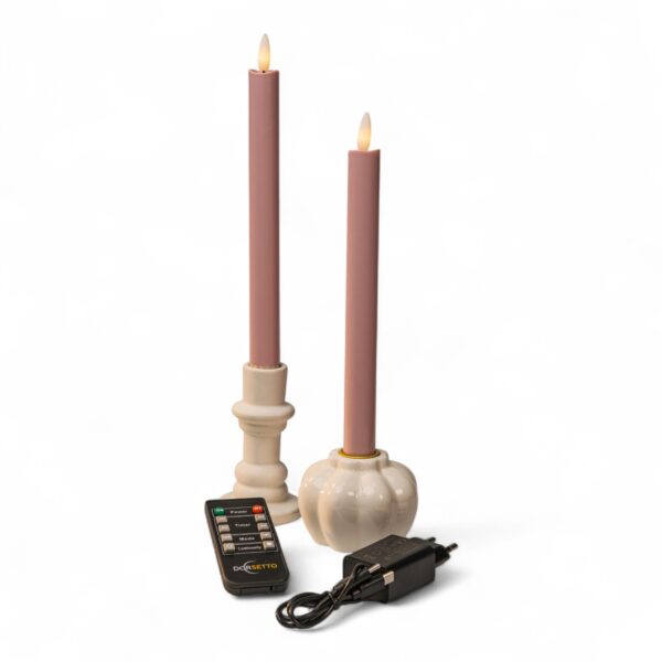 To lyserøde LED middagslys i hvide holdere med fjernbetjening og sort strømadapter på hvid baggrund, med realistisk flammeform.