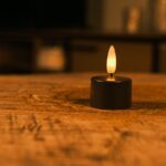 Tolv sorte genopladelige fyrfadslys med brændetid op til 400 timer og fjernbetjening står på en træoverflade og kaster et varmt skær. Den blødt slørede baggrund skaber en hyggelig og afslappet stemning.