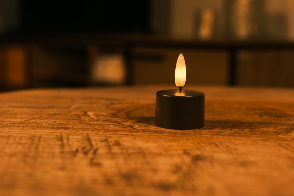 Tolv sorte genopladelige fyrfadslys med brændetid op til 400 timer og fjernbetjening står på en træoverflade og kaster et varmt skær. Den blødt slørede baggrund skaber en hyggelig og afslappet stemning.