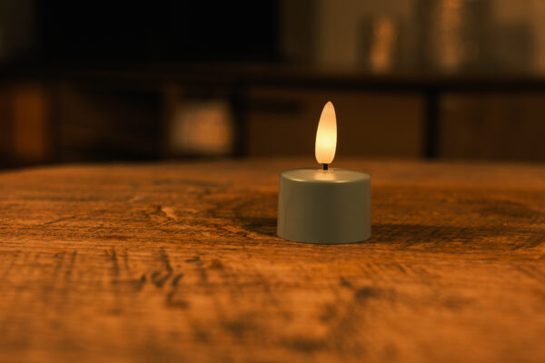 Sæt med 12 olivengrønne LED-fyrfadslys med fjernbetjening står på en træoverflade og giver et varmt, blødt skær i op til 400 timer, hvilket skaber en hyggelig og intim stemning.