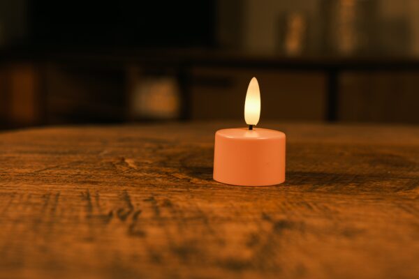 Et sæt med 12 rosa genopladelige fyrfadslys med blød gul LED-flamme og en fjernbetjening står på et træbord. Hvert fyrfadslys kan lyse op til 400 timer og skaber stemningsfuld belysning i hjemmet.