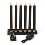 Seks sorte elektroniske stearinlys med flammeformede lys er arrangeret i en rektangulær sort base. Foran er der en fjernbetjening og en strømadapter på en hvid baggrund.
